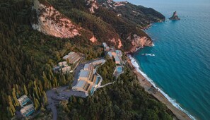 An aerial view of a coastal resort with multiple buildings, a swimming pool, and a beach. - Ella Alkyna – Adults Only (Corfu)