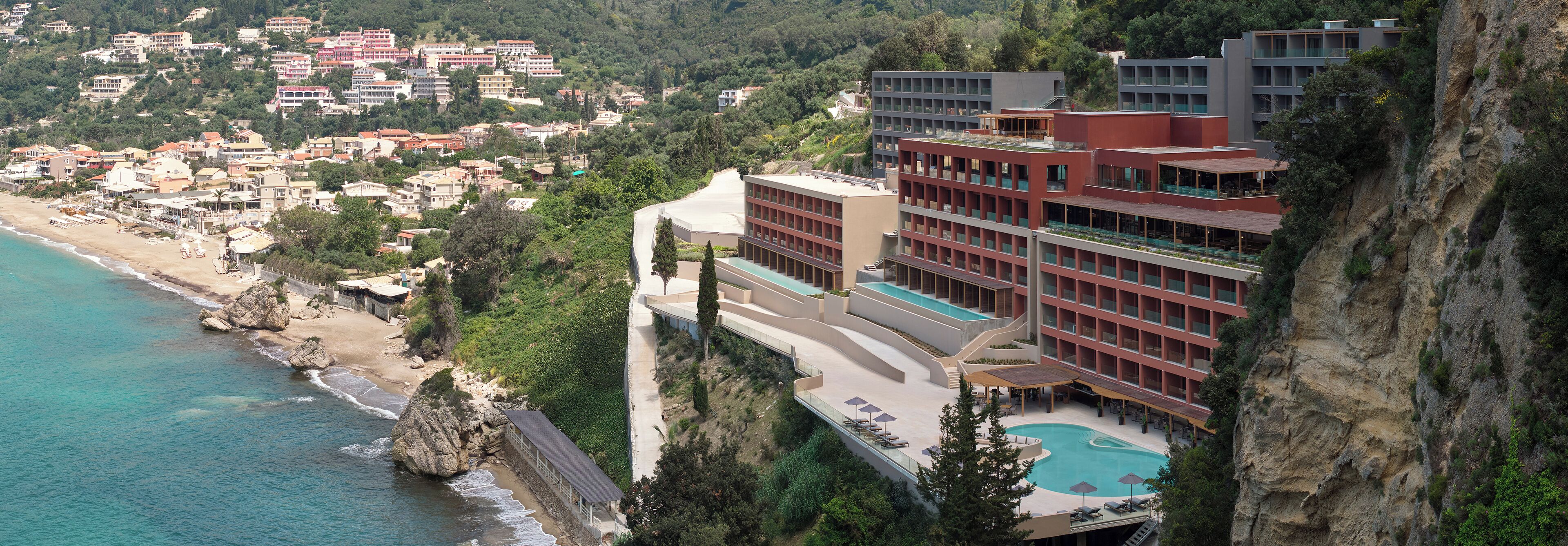 Un hotel con piscina en la azotea, situado en un acantilado con vistas a una playa y un pueblo.