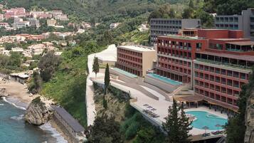 Un hotel con piscina en la azotea, situado en un acantilado con vistas a una playa y un pueblo.