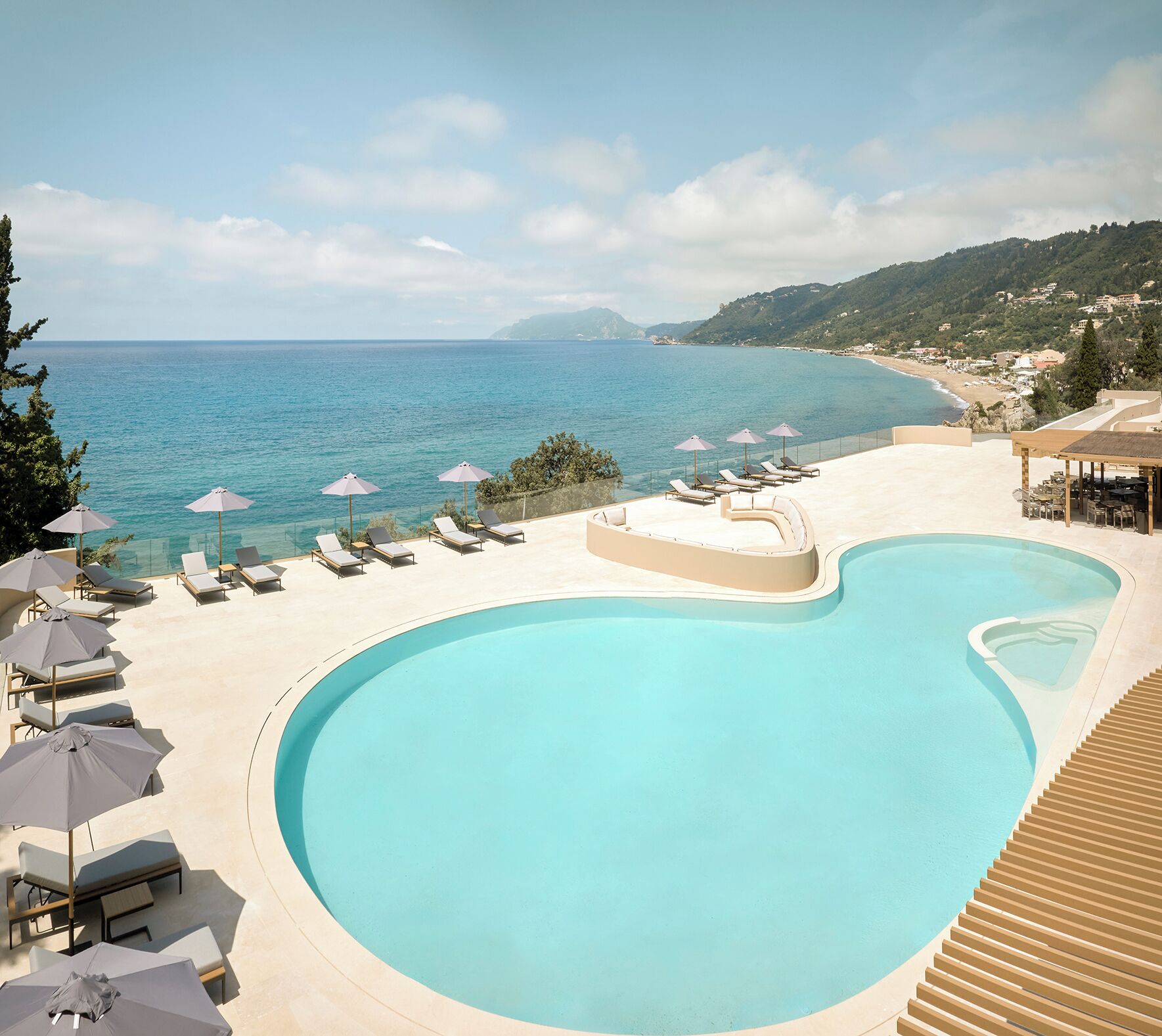 A pool with lounge chairs and umbrellas, overlooking a coastal area with a clear sky.