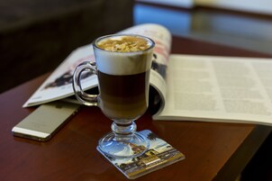 Una taza de café sobre un posavasos con diseño de paisaje urbano, un teléfono inteligente y una revista sobre una mesa de madera.