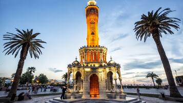 A historic tower with a clock, surrounded by palm trees and a paved plaza.