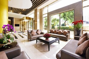 A modern lobby with a sofa set, a coffee table, and large windows offering a view of greenery and a building.