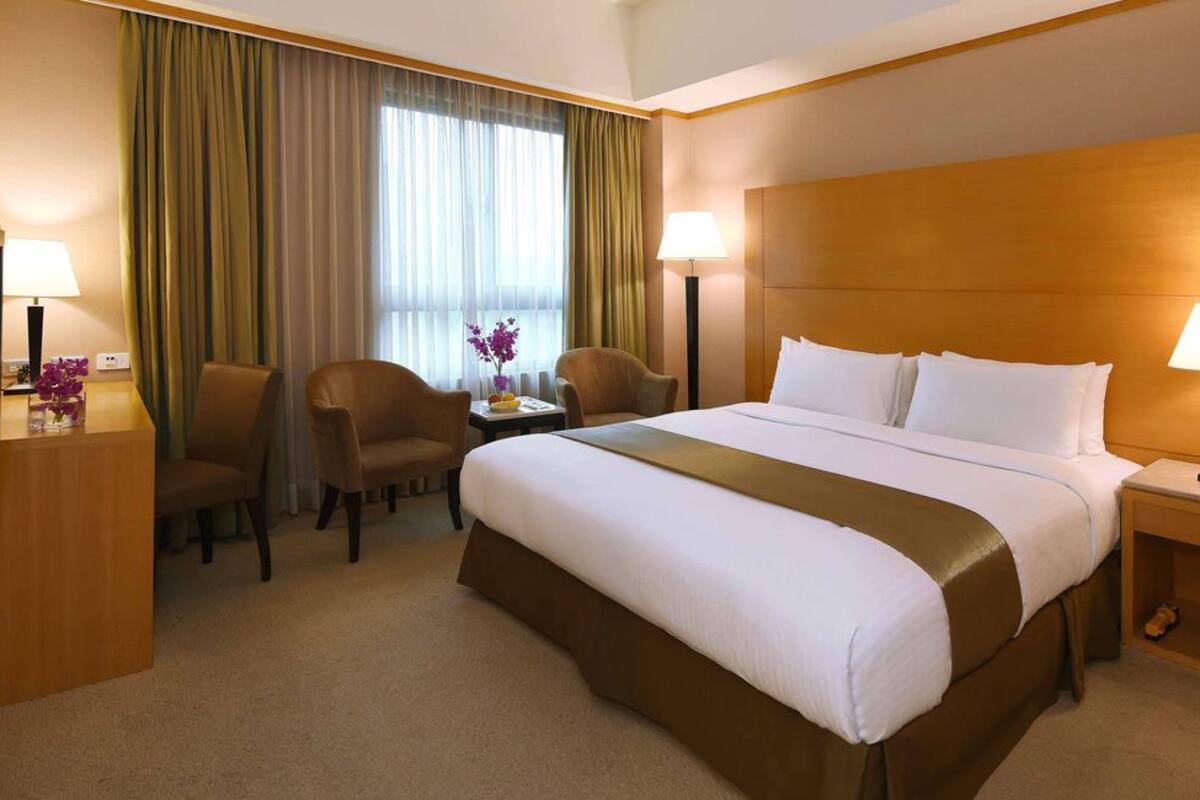 A hotel room with a large bed, two bedside tables, a desk with a chair, a TV, and a window with curtains.