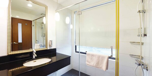 Une salle de bain moderne avec un grand miroir, un lavabo, une douche en verre et une serviette accrochée à la porte.