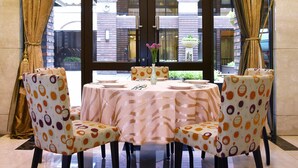 Un coin repas avec une table et des chaises, une vue à travers une porte vitrée et un bâtiment en briques à l’extérieur.