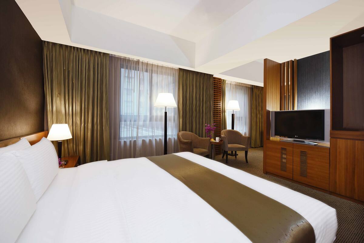 A hotel room with a large bed, two armchairs, a TV, and a desk with a lamp.