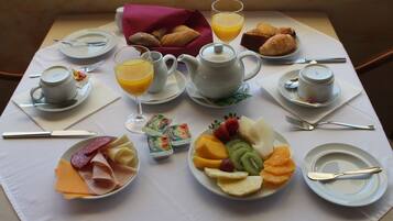 Un desayuno servido con platos de comida, una tetera, tazas y un vaso de zumo de naranja.