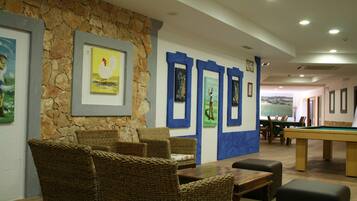 Uma sala de bilhar com móveis de vime, obras de arte emolduradas nas paredes e uma parede de destaque em pedra.
