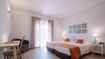 A hotel room with a bed, a desk, a chair, and a window with curtains.