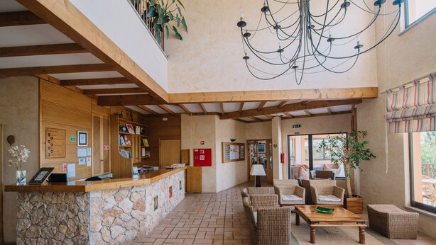A lobby with a stone reception desk, wicker furniture, and a chandelier. - Quinta dos Poetas Nature Hotel & Apartments (Olhao)