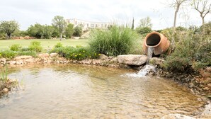 A small pond with a clay pipe releasing water, surrounded by rocks and plants, with a building in the background. - Quinta dos Poetas Nature Hotel & Apartments (Olhao)