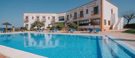 Una piscina al aire libre, sombrillas, sillones reclinables de piscina