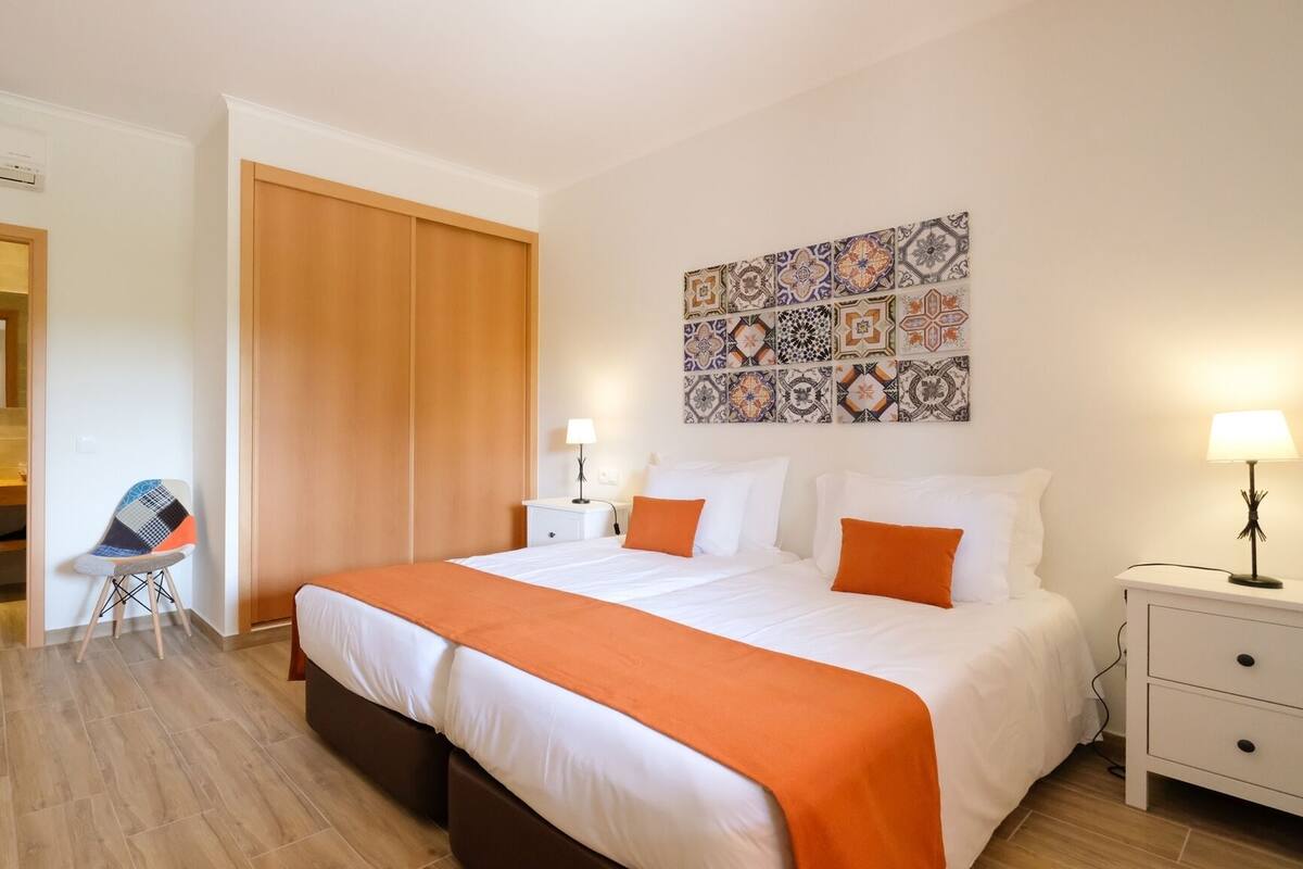 Een hotelkamer met een bed, nachtkastje, stoel en een badkamer door een open deur zichtbaar.