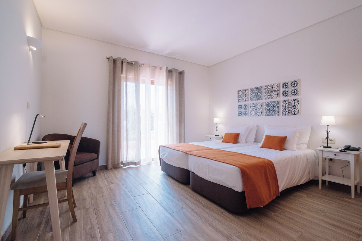 A hotel room with a bed, a desk, a chair, and a window with curtains.