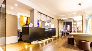 Un área de recepción moderna con suelo de madera, un mostrador de recepción y un espacio de espera con taburetes.