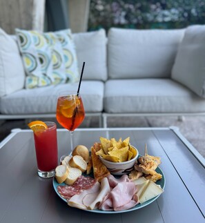 A table with a plate of food, a drink, and a couch in the background. - Spa Hotel Parigi 2 (Dalmine)