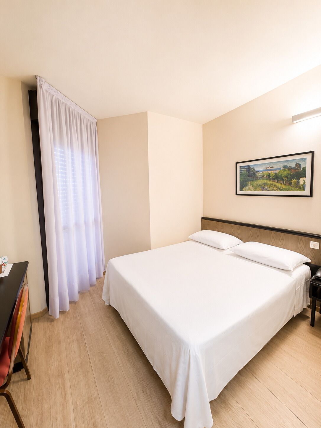 Une chambre d’hôtel avec un lit, une table de chevet, un bureau avec une chaise et un tableau au mur.