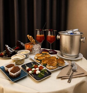 A table set with various food items, including pastries, a fruit platter, and drinks, with a metal container and utensils on the table. - Spa Hotel Parigi 2 (Dalmine)