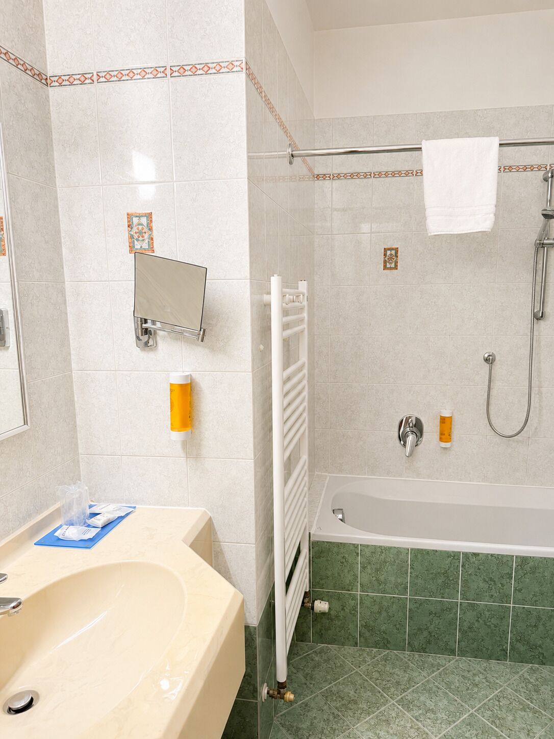 A bathroom with a bathtub, a towel rack, a mirror, and a hand sanitizer dispenser.