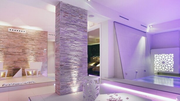 Un área de spa moderna con pared de piedra, mostrador de recepción y zona de estar con sillas.