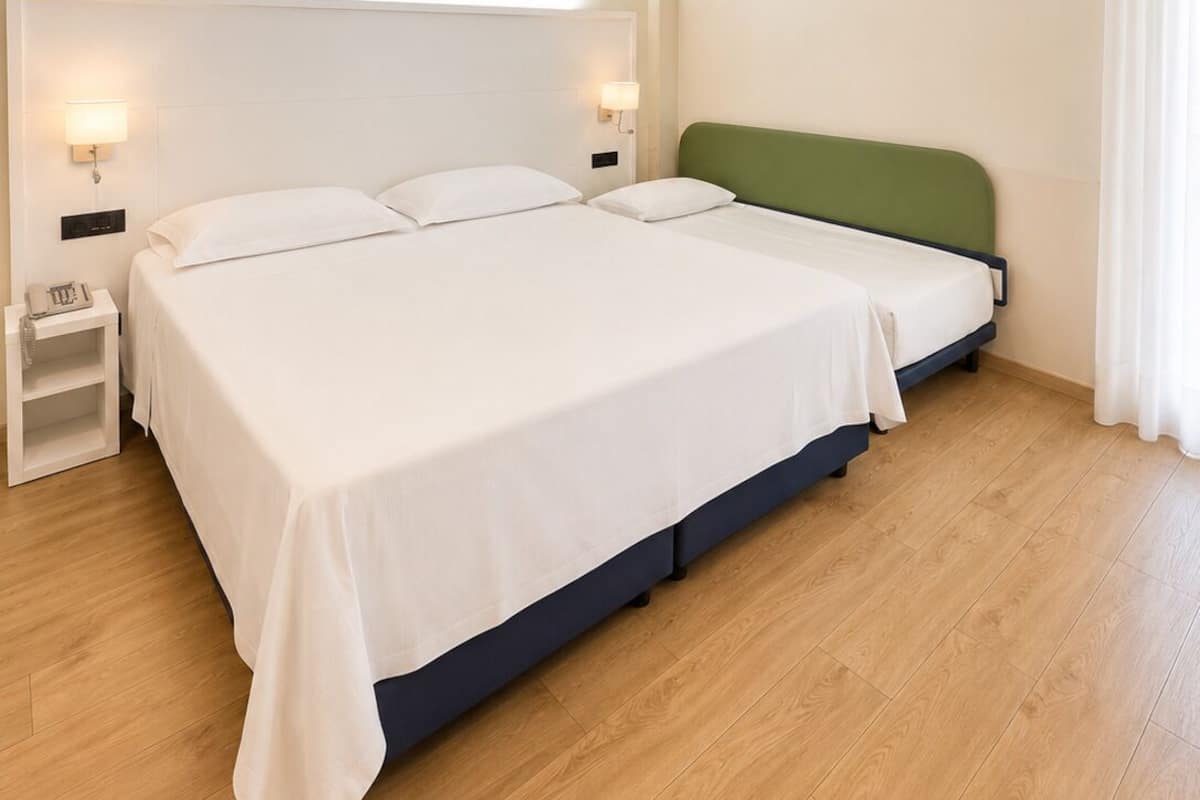 A hotel room with a large bed, bedside tables, and a green headboard.