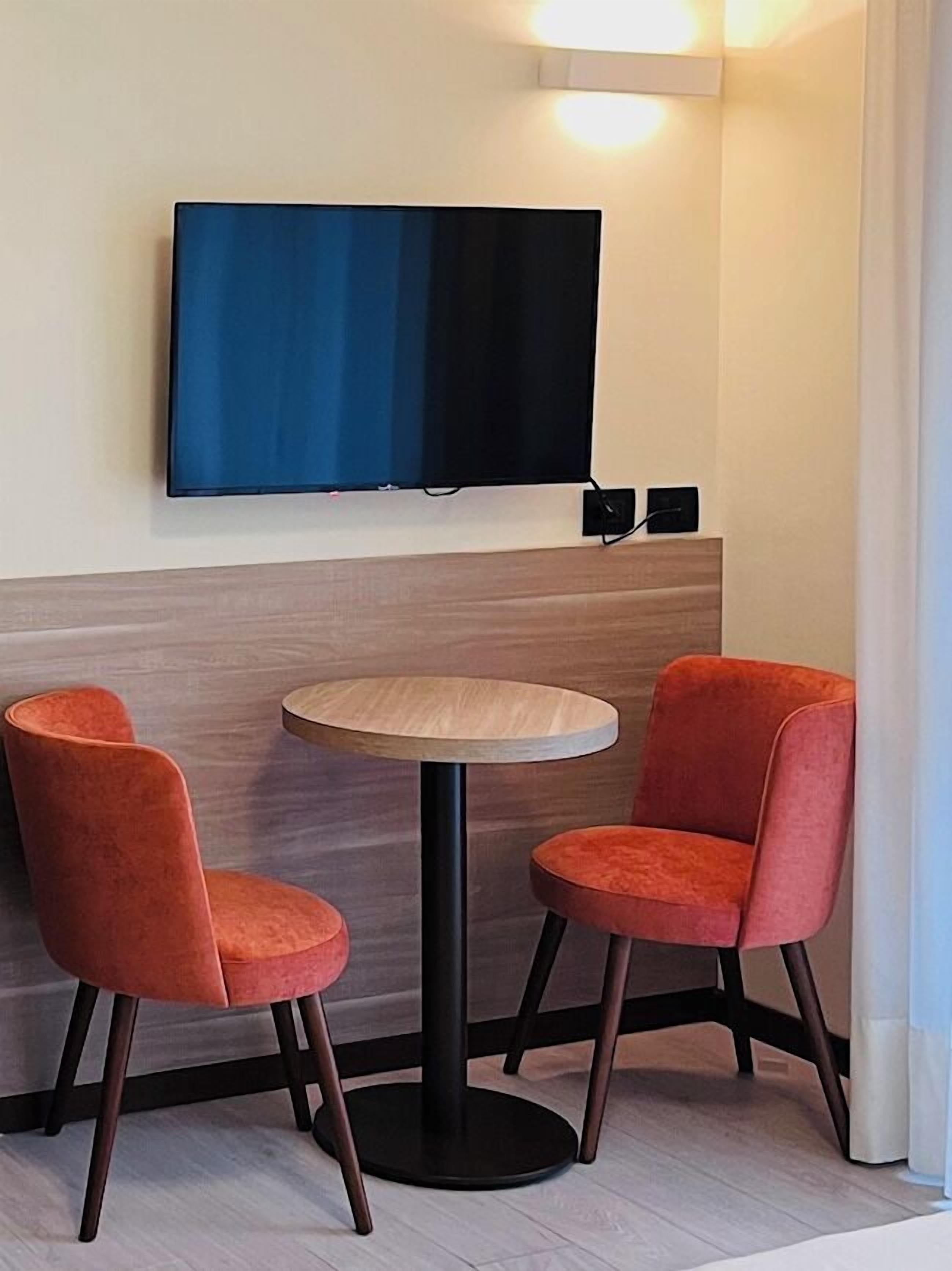 Ein Eckzimmer mit einem flachbildfernseher an der Wand, einem runden Holztisch und zwei orangefarbenen Stühlen.