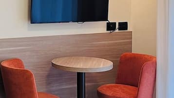 Ein Eckzimmer mit einem flachbildfernseher an der Wand, einem runden Holztisch und zwei orangefarbenen Stühlen.