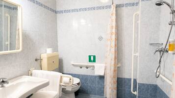 Une salle de bain équipée de toilettes, d’un lavabo, d’une douche et d’une barre d’appui.