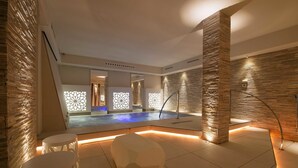 Un moderno espacio de spa con piscina, asientos geométricos y paredes de piedra.