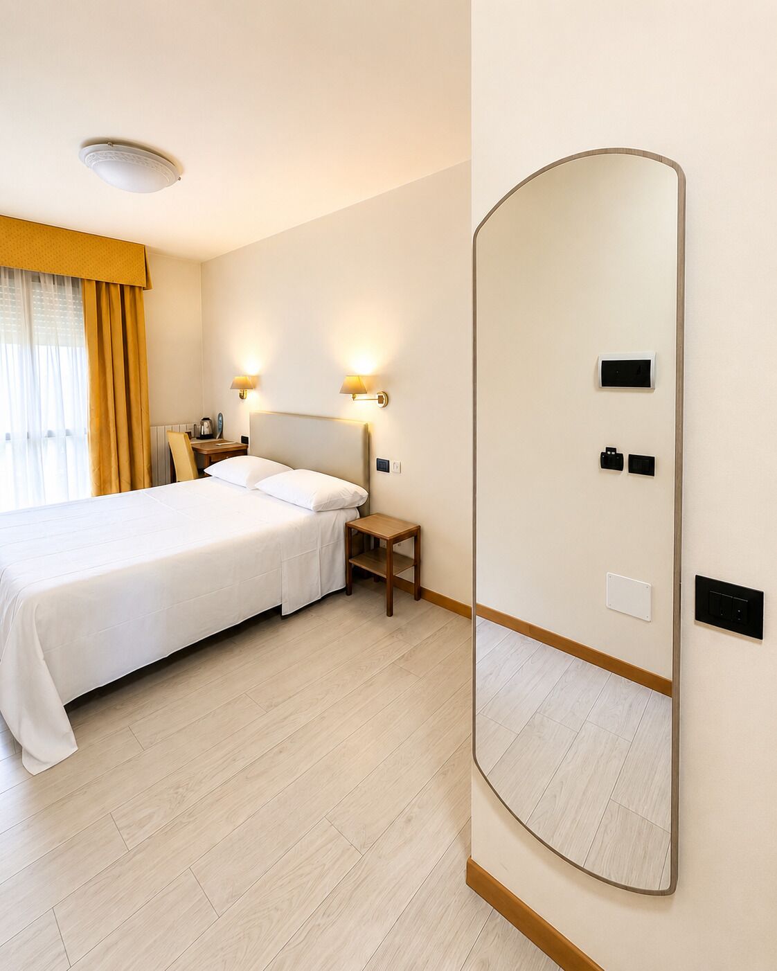 A hotel room with a bed, bedside tables, a mirror, and a light fixture.