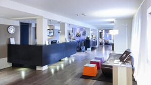 Un moderno vestíbulo de hotel con una recepción, un reloj y un comedor al fondo.
