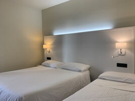 Una camera d'albergo con due letti, entrambi con lenzuola bianche, e due lampade ai comodini.