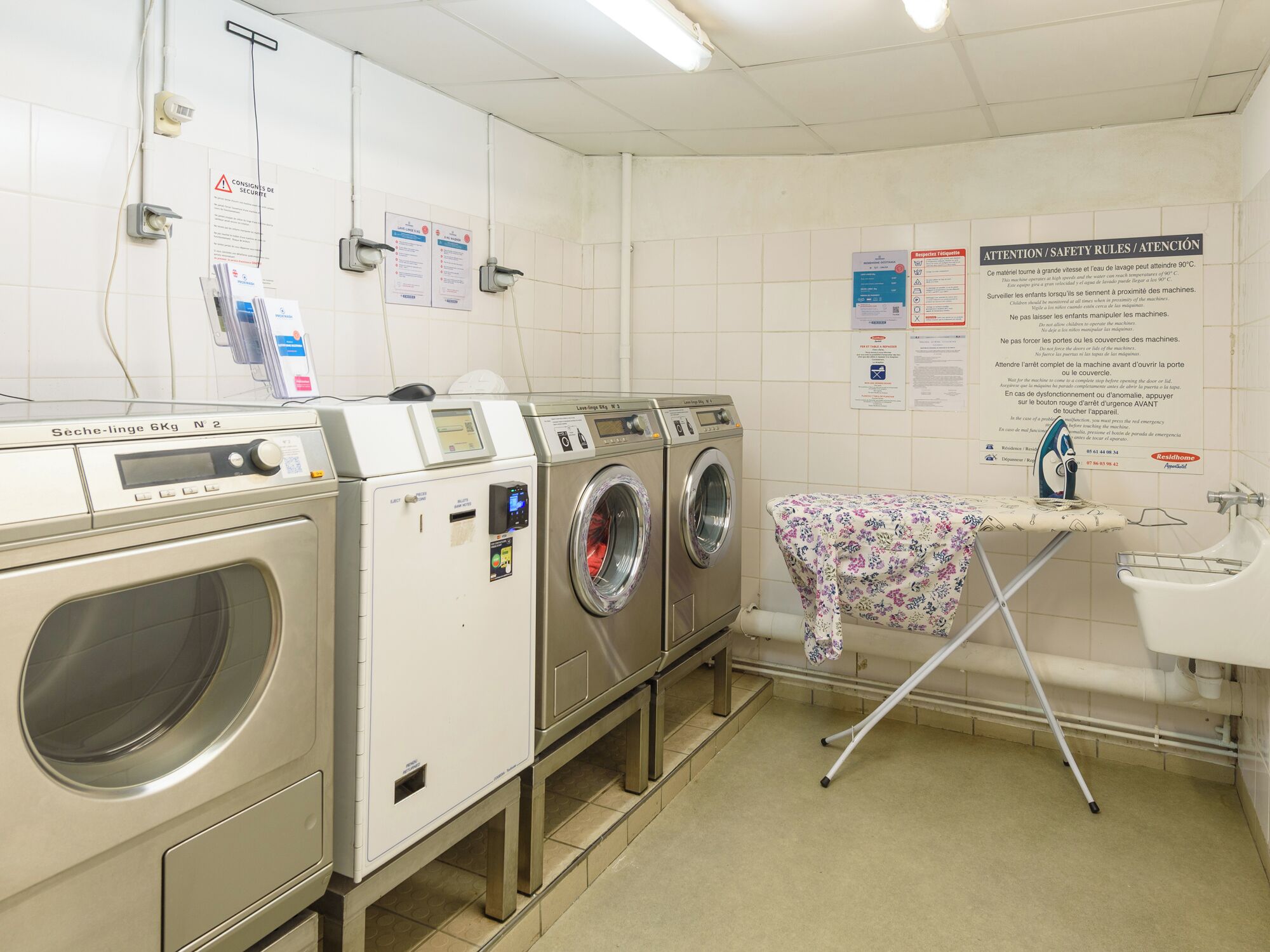 A laundry facility with multiple washing machines, a drying rack, and safety instructions on the walls.