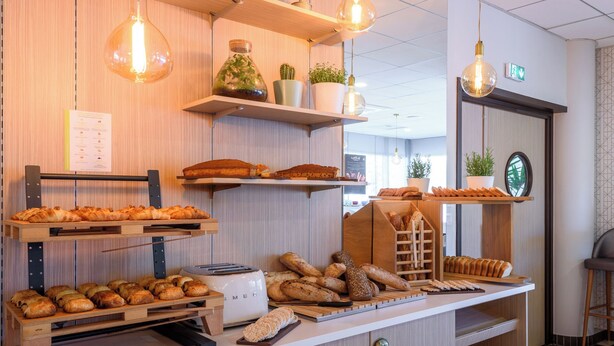 A bakery display with various breads and pastries, wooden shelves, and hanging light bulbs. - Residhome Toulouse Occitania (Toulouse)