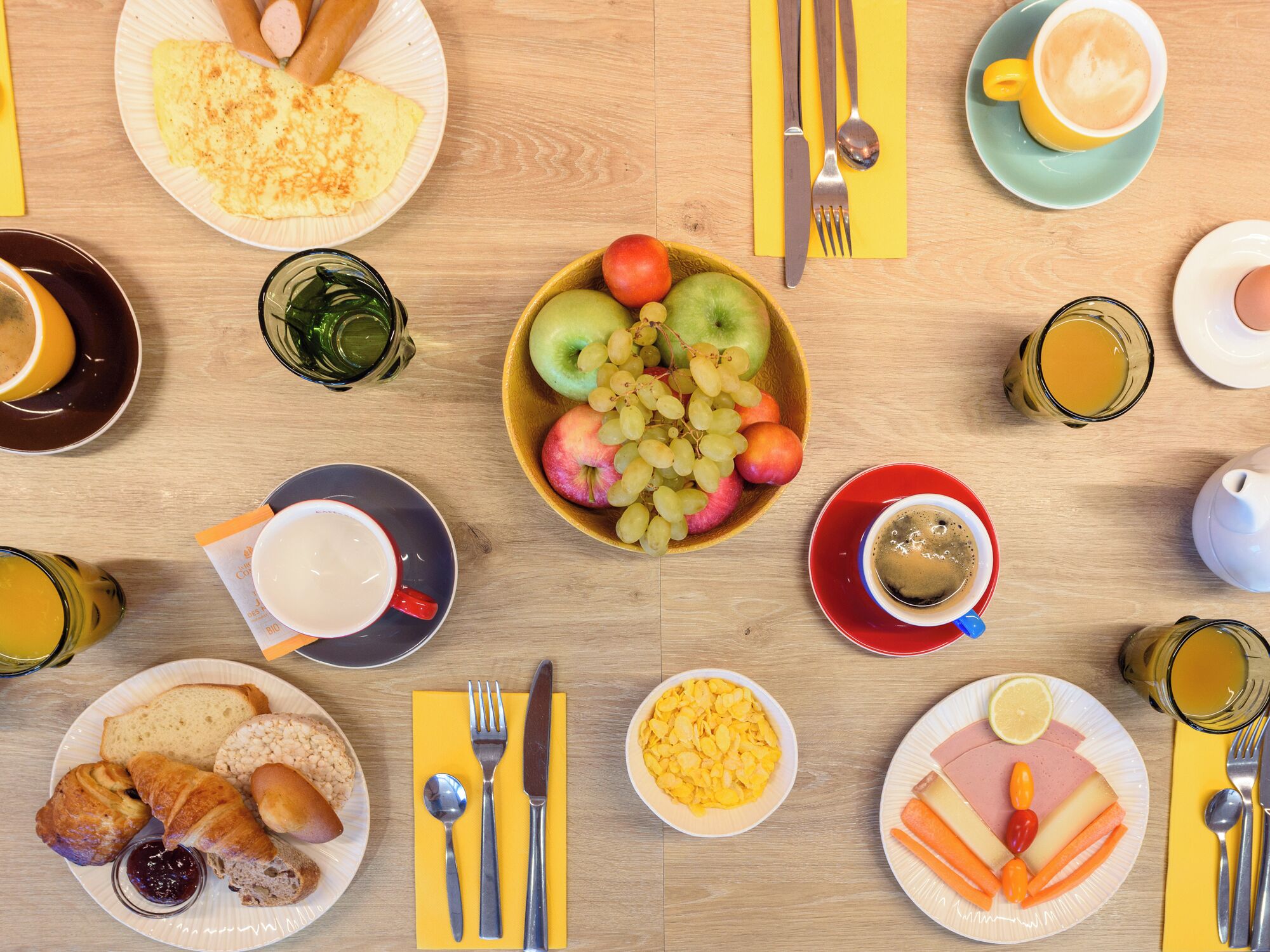 A breakfast table with various food items, utensils, and drinks.