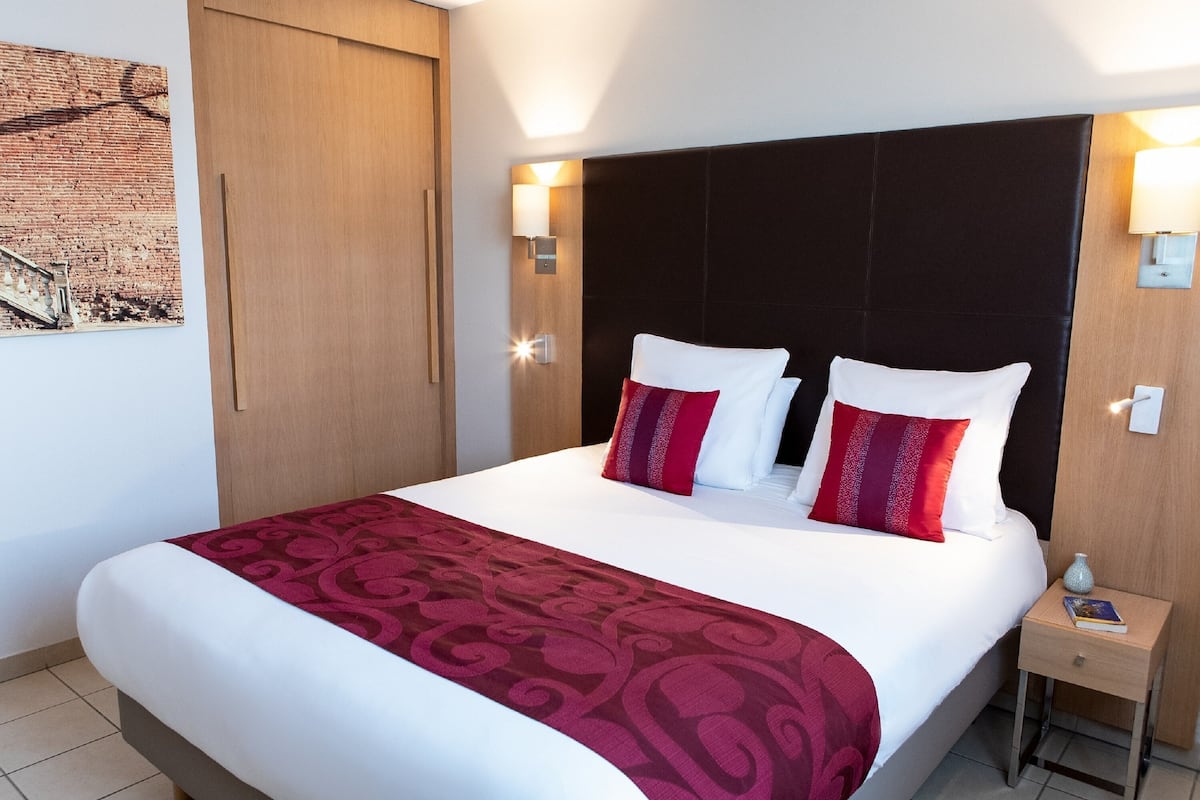 A neatly made bed with a patterned bedspread, a dark headboard, and two bedside lamps.