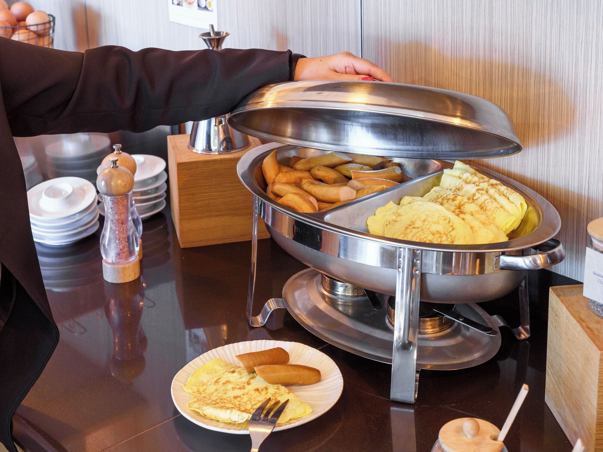 Montaje de bufé con diversos alimentos, incluyendo crepes y pasteles, sobre una bandeja de acero inoxidable.