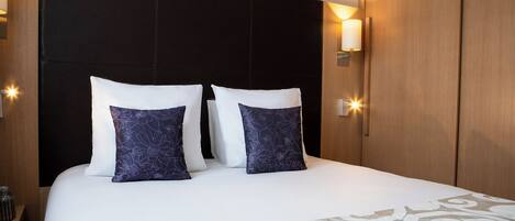 A neatly made bed with white and patterned pillows, a decorative throw, and wall-mounted lights.