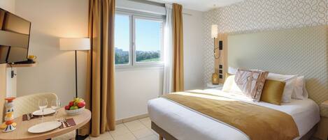 Una habitación de hotel con una cama, un escritorio con silla, un televisor y una ventana con cortinas.
