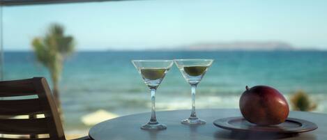 A table with two martini glasses and a fruit on a round table, overlooking a body of water.