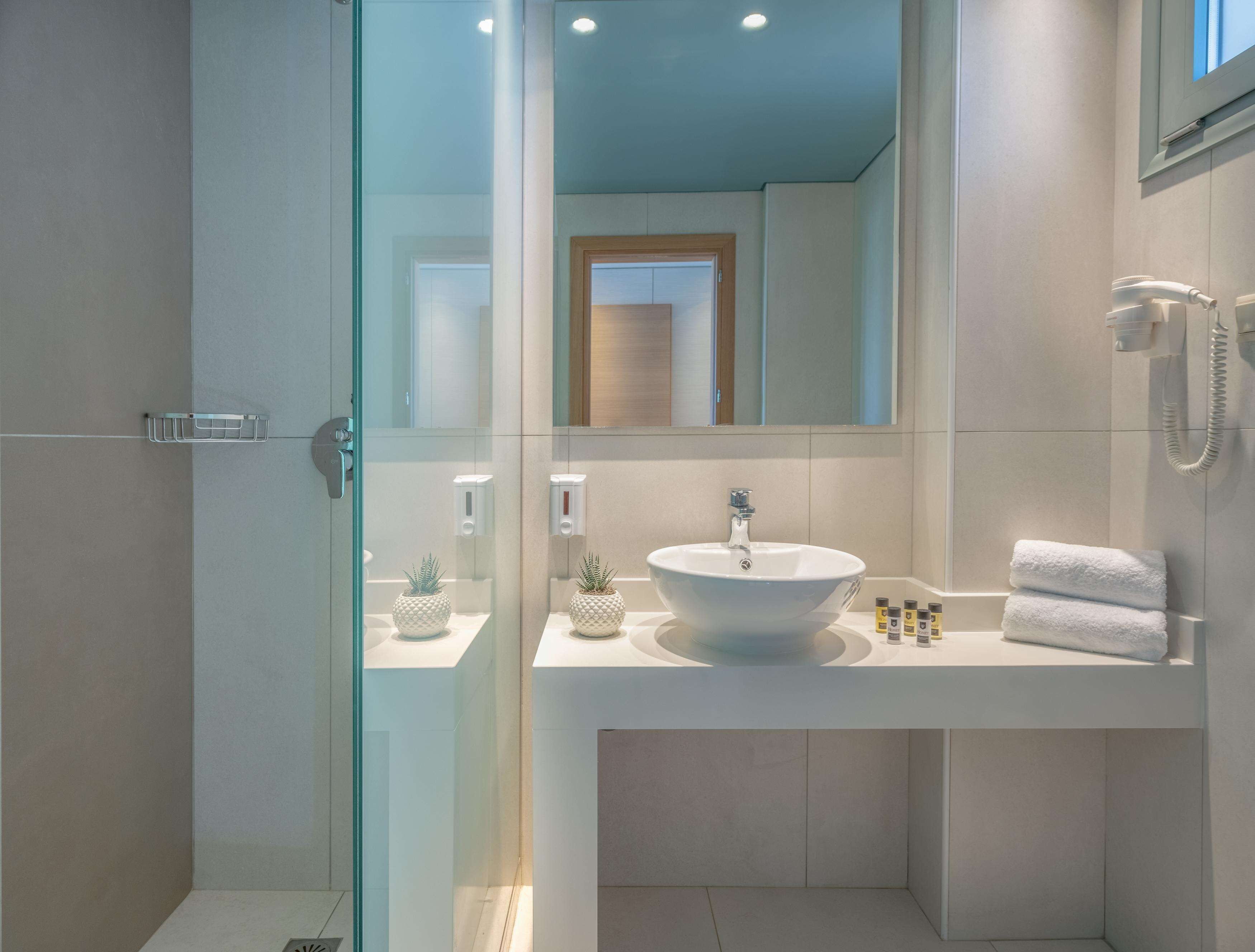 Un baño moderno con cabina de ducha de vidrio, un lavabo blanco con forma redonda y un espejo sobre él.