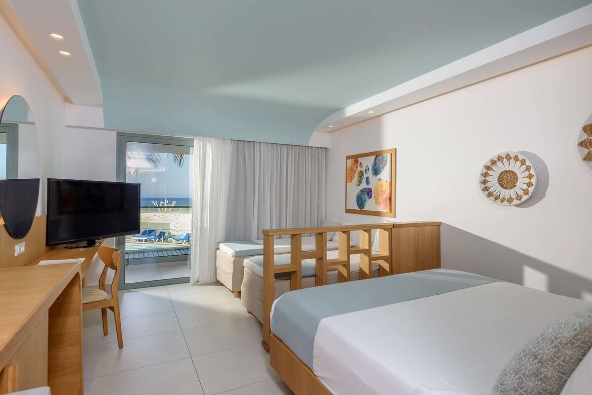 A hotel room with a bed, a desk with a TV, a chair, a balcony with a view, and decorative wall art.