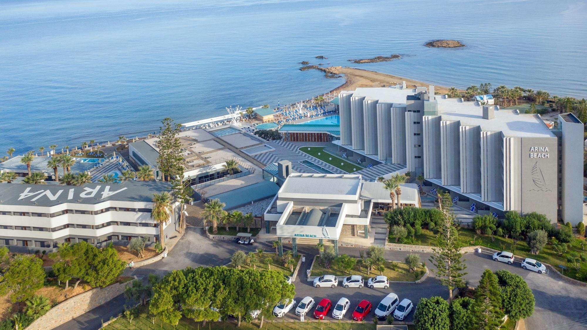 A coastal hotel with a swimming pool, parking area, and a view of the sea.