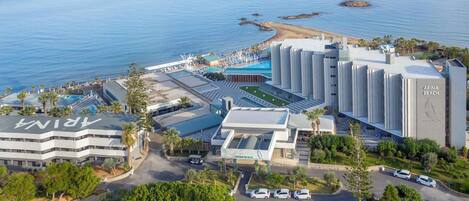 A coastal hotel with a swimming pool, parking area, and a view of the sea.