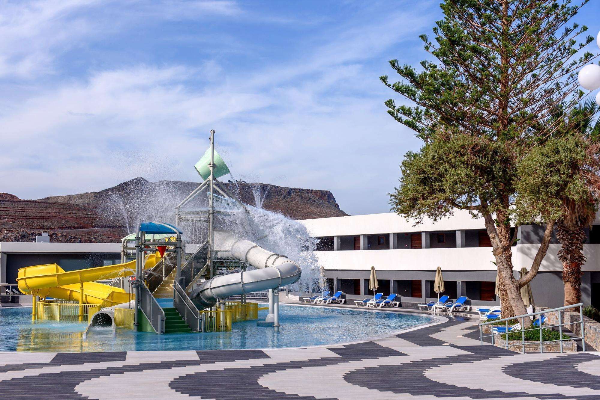 A pool area with a water slide, a fountain, and lounge chairs.