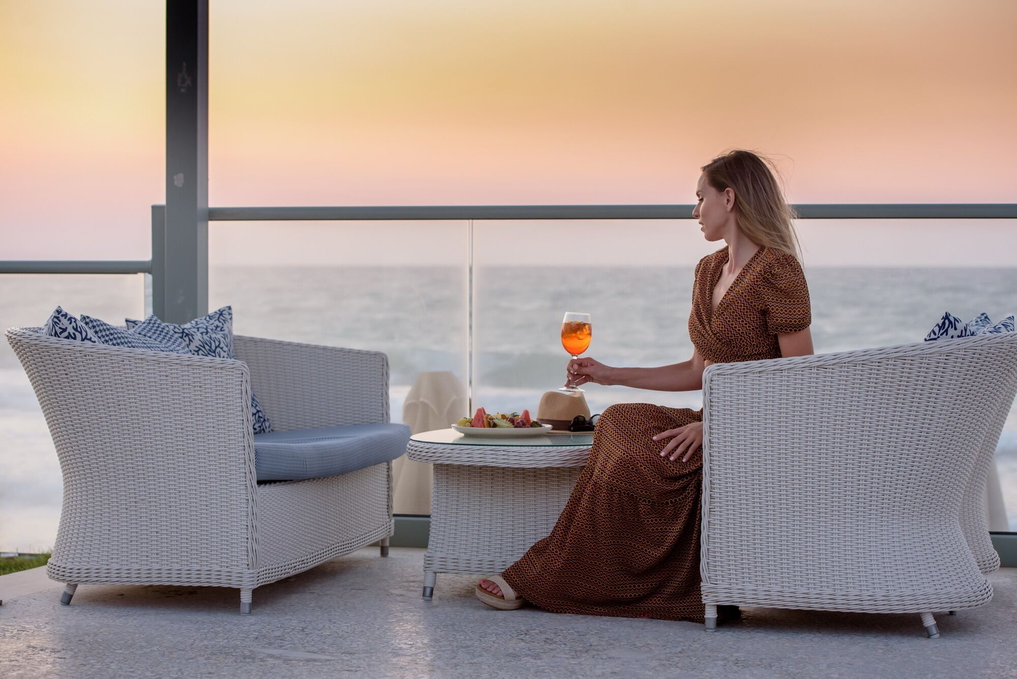 Uma pessoa sentada à mesa com um copo de bebida, com vista para um corpo de água.