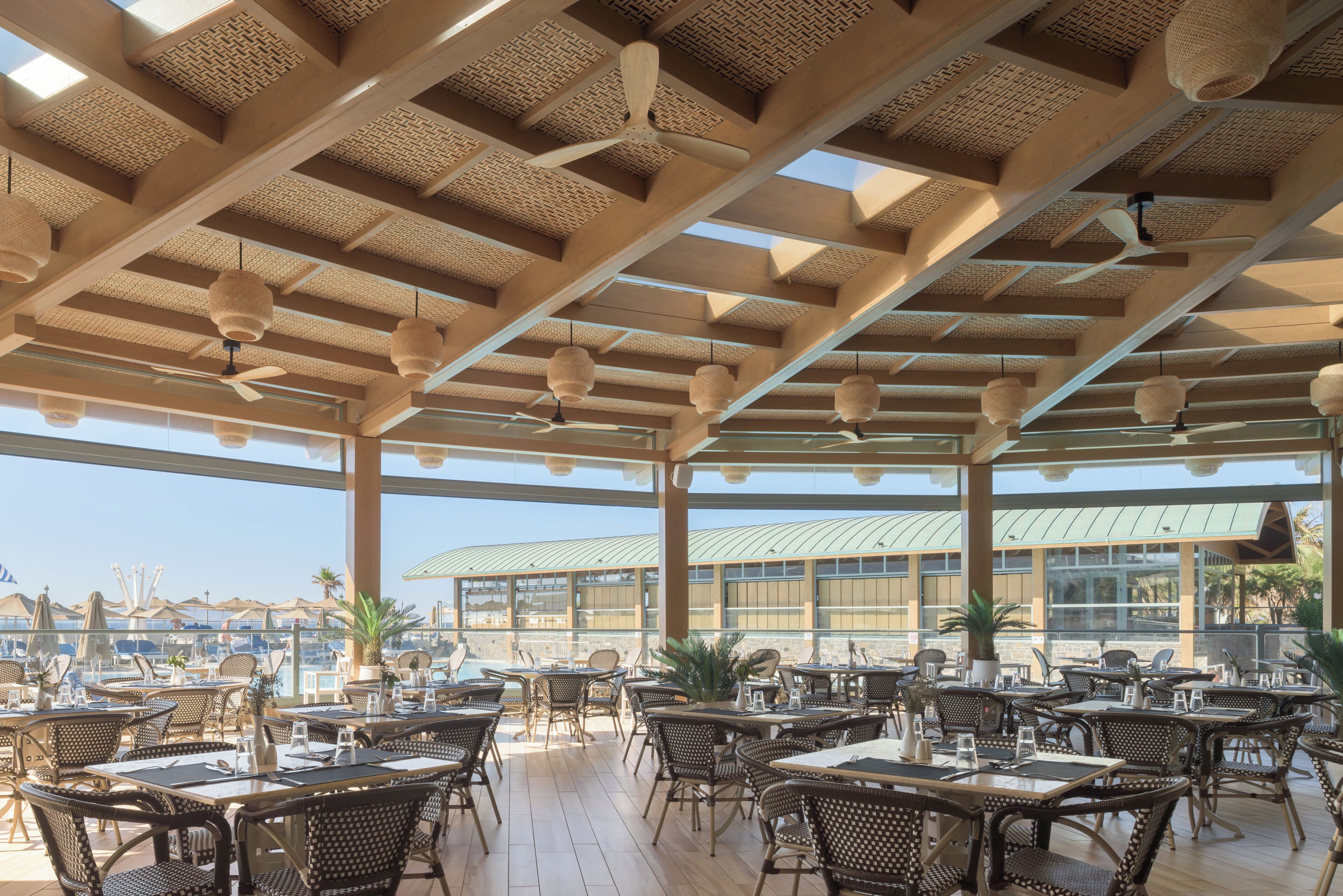 Zona pranzo all'aperto con mobili in vimini, ventilatori a soffitto e vista sulla città.