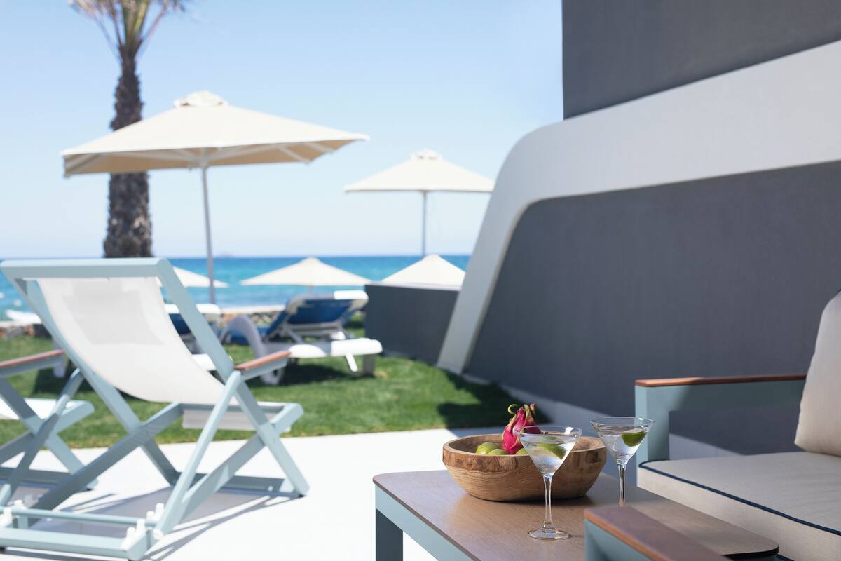 A poolside area with lounge chairs, umbrellas, a wooden table with a drink, and a view of the ocean.
