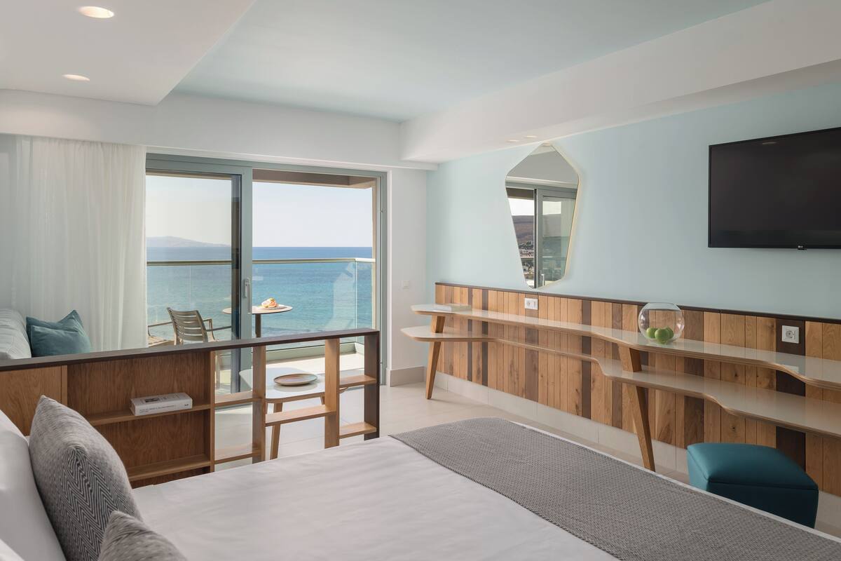 A modern hotel room with a balcony, a large bed, a desk, and a TV.